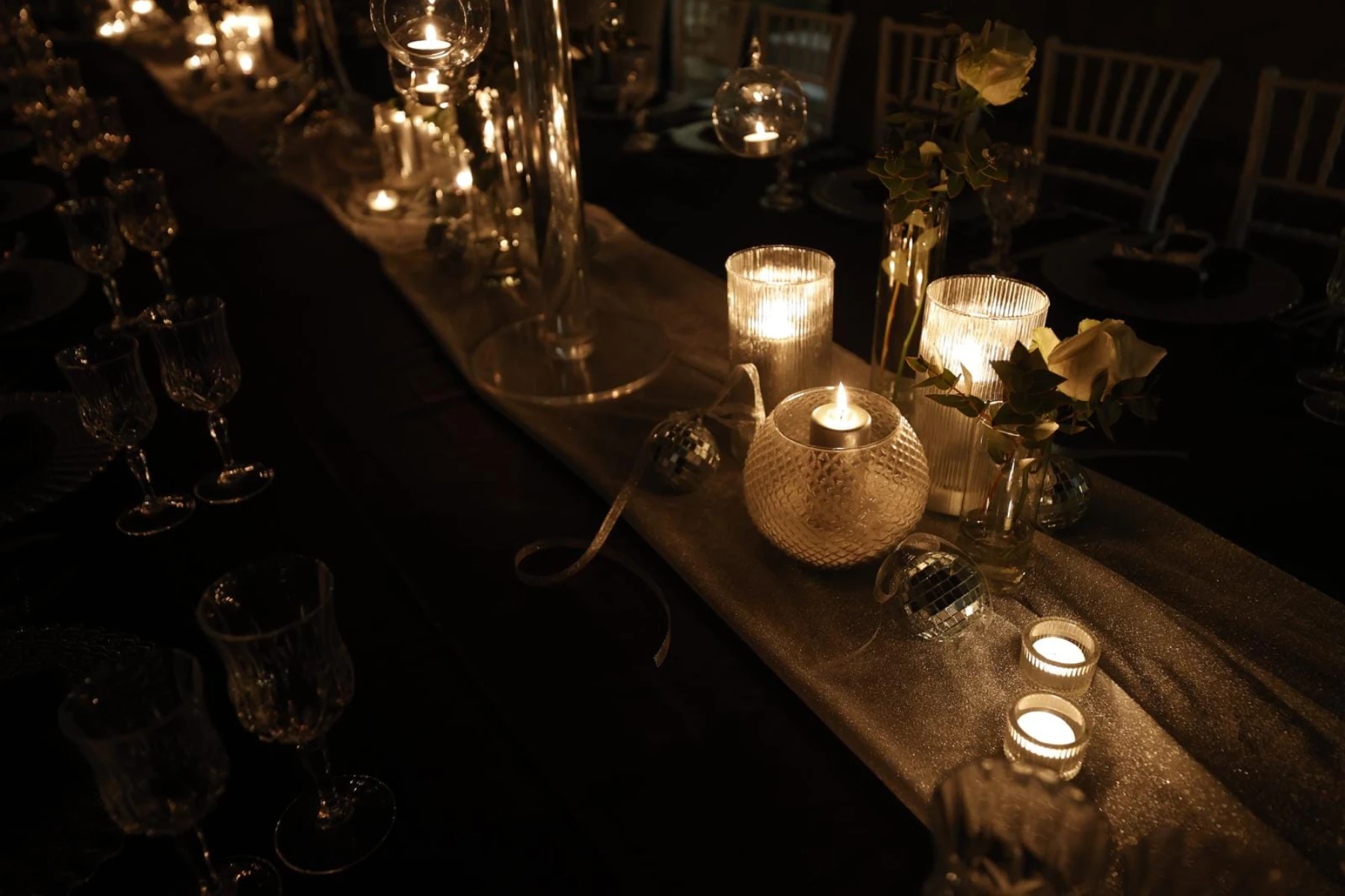 Dettaglio della tavola: candele, rose bianche e sfere a specchio sul runner